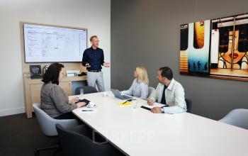 A modern conference room at Teleportboulevard 110, Amsterdam Sloterdijk, where business professionals are engaged in a meeting. Ideal office space rental featuring a large table and digital presentation screen.