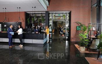 Professionals engaging in conversation at a reception area of an office space available for rent at Teleportboulevard 110, Amsterdam Sloterdijk. The office features a modern design with plants and seating.