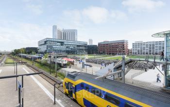 View of the office building at Teleportboulevard 110, Amsterdam Sloterdijk, with nearby train tracks and a bustling urban setting, ideal for office space rental.
