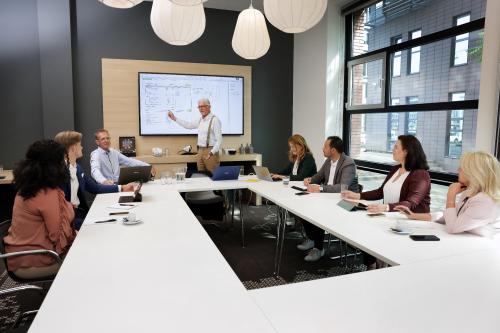A team engaged in a meeting around a modern conference room table at Teleportboulevard 110, with large windows providing natural light in Amsterdam Sloterdijk. A perfect office space rental opportunity.