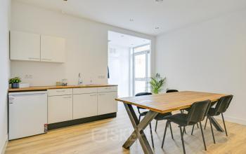 Bright office space in Amsterdam Sloterdijk, featuring a minimalist kitchen area and a wooden table with chairs, perfect for workspace needs or small meetings. Ideal for office space rental.