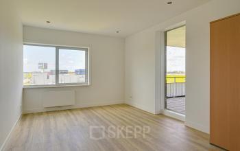 Bright office space available for rent in Amsterdam Sloterdijk at Tijnmuiden 59, featuring wooden flooring, a large window with natural light, and an accessible balcony.