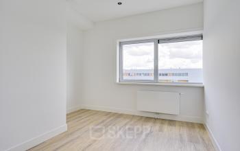 A bright, empty office room with wooden flooring and a large window, located at Tijnmuiden 59, Amsterdam Sloterdijk, ideal for office space rental.
