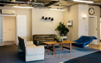 Interior view of a furnished office lounge at Kabelweg 24, Amsterdam Sloterdijk, featuring modern seating and a coffee table. Ideal for office space rental.