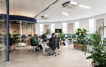 Modern office space at Arlandaweg 92, Amsterdam Sloterdijk, featuring workstations, large windows, and indoor plants. Office workers engaged in tasks. Office space rental available.