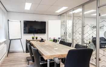 Conference room at Arlandaweg 92, Amsterdam Sloterdijk, with modern furnishings, a large wooden table, black chairs, flipchart, and a wall-mounted TV.
