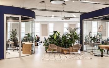 Modern open floorplan office space at Arlandaweg 92, Amsterdam Sloterdijk, with glass partitions, seating area, lush indoor plants, and people working.