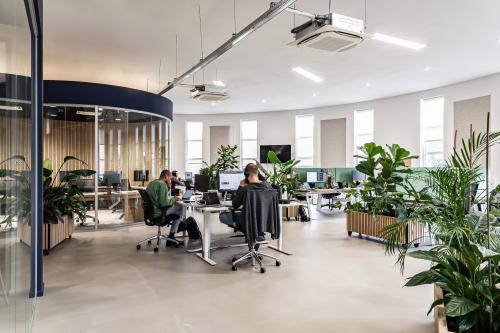 Modern office space at Arlandaweg 92, Amsterdam Sloterdijk, featuring workstations, large windows, and indoor plants. Office workers engaged in tasks. Office space rental available.