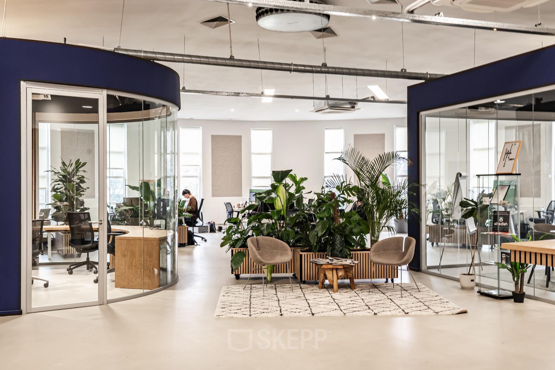 Modern open floorplan office space at Arlandaweg 92, Amsterdam Sloterdijk, with glass partitions, seating area, lush indoor plants, and people working.