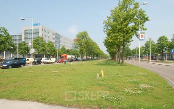 Exterior view of the office building located at Elektronstraat 15, Amsterdam Sloterdijk, Amsterdam, showing a spacious grassy area alongside the street and nearby buildings.