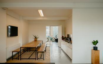 Bright office interior at Overtoom 141, Amsterdam West, featuring a modern kitchen area with a long wooden table, benches, and indoor plants, ideal for office space rental.