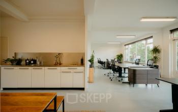 Bright office space at Overtoom 141, Amsterdam West featuring modern furniture, large windows, and a kitchenette area. Ideal for office space rental with plenty of natural light and a clean design.
