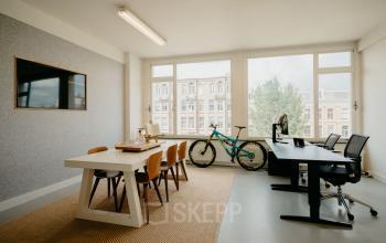 Amsterdam West office to rent at Overtoom 141 featuring a bright room with a desk, chairs, and a bicycle by the window.