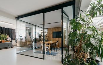 Bright office space rental at Overtoom 141, Amsterdam West, with glass partitions and modern furnishings, with a person working at a desk inside.