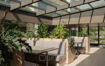 Bright and modern office space rental at Nachtwachtlaan 20, Amsterdam West, featuring a skylight, plants, and seating booths for a refreshing work atmosphere.