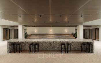 Modern office space in Amsterdam West at Nachtwachtlaan 20, featuring a spacious open area with a terrazzo table and bar stools, ideal for office space rental.