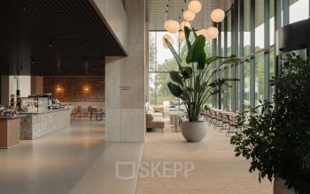 Modern office interior at Nachtwachtlaan 20, Amsterdam West, featuring large windows, a lounge area, and plants. Ideal for those seeking office space rental with natural light.