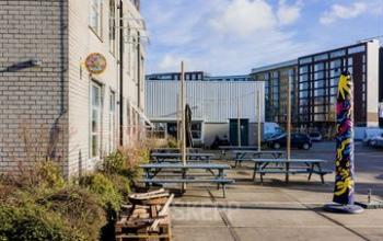 Outdoor area at Rigakade 10, Amsterdam West, showcasing picnic tables and modern art installation, ideal for casual meetings or breaks. Ideal office space rental opportunity.