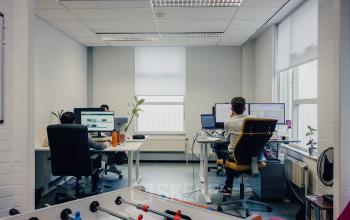 Modern office space rental at Rigakade 10 in Amsterdam West, featuring an open workspace with desks, plants, and a foosball table, ideal for collaborative work environments.