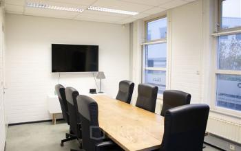 Modern office to rent at Rigakade 10, Amsterdam West features a cozy conference room with a long wooden table, black office chairs, and a wall-mounted TV, offering a professional meeting space.