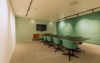 Modern conference room with a large table, green chairs, and a wall-mounted screen, ideal for office space rental at Kon. Wilhelminaplein 4 in Amsterdam West.