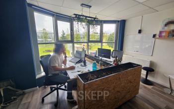 Office to rent at Gyroscoopweg 23-25, Amsterdam Westpoort, featuring a work desk with computer monitors and large windows with a view of a green landscape.