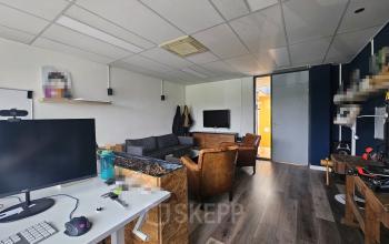 Interior view of a furnished office space at Gyroscoopweg 23-25, Amsterdam Westpoort, with multiple desks, chairs, a couch, and a TV.