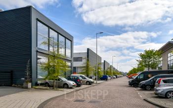 Exterior view of the modern office building at Poortland 242, located in Amsterdam Westpoort, showcasing ample parking space under a clear blue sky, suitable for office space rental.