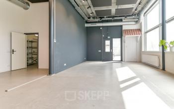Bright office space for rent in Amsterdam Westpoort, featuring large windows and modern industrial design with exposed ductwork and high ceilings.