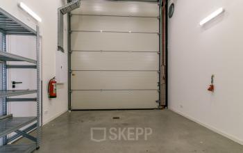 Empty warehouse-style interior at Poortland 242, Amsterdam Westpoort, featuring high ceilings, industrial lighting, and wall-mounted fire safety equipment, ideal for versatile office space rental.