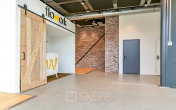 Modern office space at Poortland 242, Amsterdam Westpoort featuring an open layout with stylish brick accents and a sliding barn door. Ideal for office space rental, offering a versatile environment for businesses.