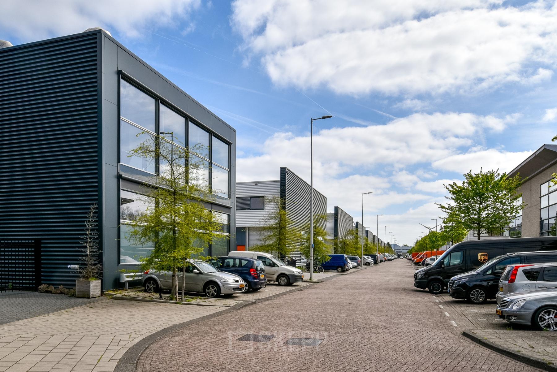 Exterior view of the modern office building at Poortland 242, located in Amsterdam Westpoort, showcasing ample parking space under a clear blue sky, suitable for office space rental.
