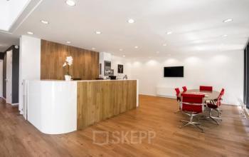 Modern office space featuring a sleek reception area and a meeting table with red chairs, available for rent at Hullenbergweg 278, Amsterdam South East.