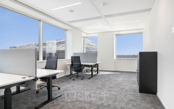 Bright office space with large windows and several desks and chairs, available for rent at De Entree 201, Amsterdam South East.