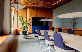 Elegant office space featuring a long wooden table, blue chairs, a large TV, and potted plant at Bijlmerplein 888, ideal for office space rental in Amsterdam South East.