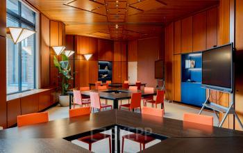 Modern office space with wood paneling, vibrant orange chairs around tables, and large screens, ideal for office space rental in Amsterdam South East.