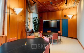 Bright office space at Bijlmerplein 888, Amsterdam South East, featuring stylish wooden walls, modern lighting, and neatly arranged tables for office rental opportunities.