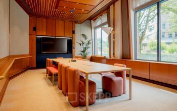 A furnished office space at Bijlmerplein 888, Amsterdam South East, featuring a wooden conference table and chairs with a large window view, ideal for rent office space needs.