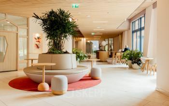 Modern office space in Amsterdam South East with stylish seating area and greenery, ideal for office space rental. Features natural light and vibrant design at Bijlmerplein 888.