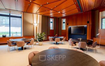 Spacious office interior at Bijlmerplein 888 in Amsterdam South East with round tables and chairs, ideal for office space rental. Features warm lighting and large windows.