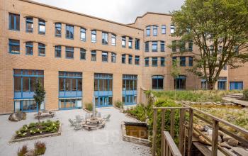 Exterior view of Bijlmerplein 888 in Amsterdam South East, showcasing a brick building and a peaceful patio. Ideal office space rental with outdoor seating options.