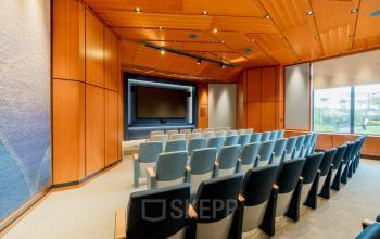 Seminar room at Bijlmerplein 888 in Amsterdam South East, featuring rows of cushioned chairs and a large presentation screen, ideal for office space rental.
