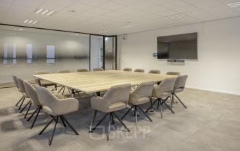 Spacious conference room in Amsterdam South East featuring a large wooden table surrounded by comfortable chairs, ideal for office space rental. Equipped with a wall-mounted screen for presentations.