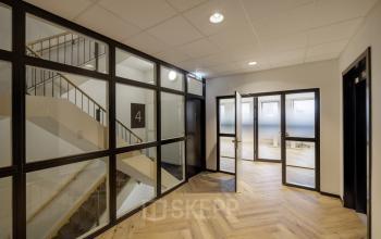 Spacious office entrance at Hogehilweg 24 in Amsterdam South East, featuring modern design elements with wooden flooring and glass partitioning, ideal for office space rental inquiries.
