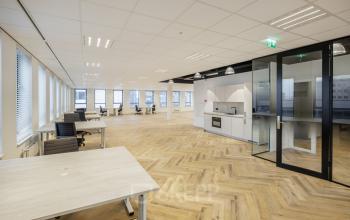 Modern open floorplan office space for rent at Hogehilweg 24 in Amsterdam South East, featuring sleek wooden flooring, abundant natural light, and a compact kitchenette.