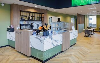 Modern reception area with marble counters and wooden accents at Hogehilweg 24, Amsterdam South East, perfect for office space rental. Open seating in the background adds a welcoming touch.