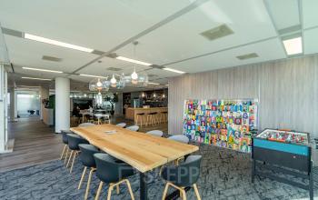 Stylish office space in Amsterdam South East with modern furnishings, featuring a long wooden table and a vibrant art display. Ideal for office space rental enthusiasts looking for a creative environment.