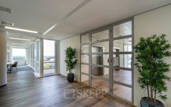 Modern office space with glass walls, potted plants, and wooden flooring at De Entree 230-266, Amsterdam South East, ideal for rent office space.