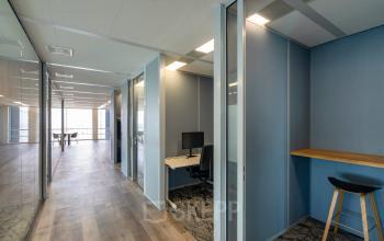 Office to rent at De Entree 230-266, Amsterdam South East, featuring a modern hallway with glass partitions, workstations with computers, and a sleek high stool area, ideal for collaboration and productivity.