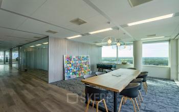 Modern office space for rent in Amsterdam South East at De Entree 230-266, featuring large windows, stylish lighting, a colorful wall art piece, and contemporary furnishings, ideal for creative working environments.